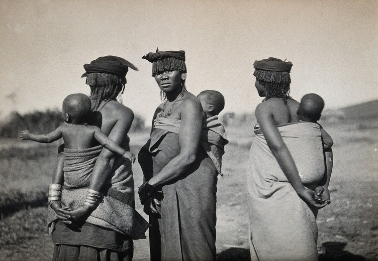 Africa: three women carrying babies on their backs in fabric slings. Photograph, 1910/1930: Credit Wellcome Collection [CC BY]