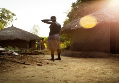 image of woman standing outside huts in uganda 
