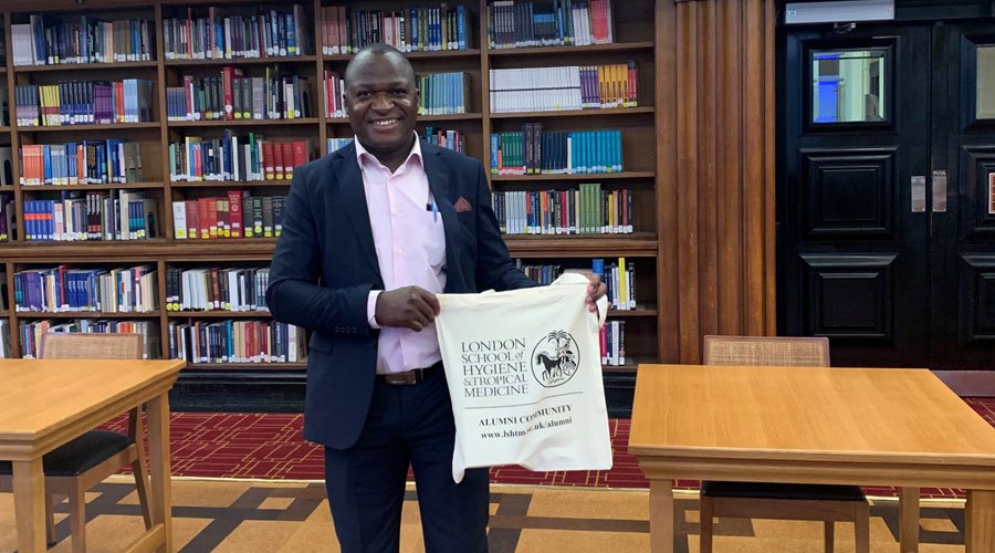 Enock Musungwini in the LSHTM Library holding an LSHTM branded bag