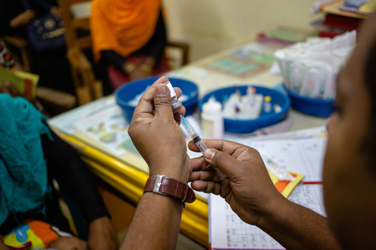 A healthcare worker drawing up a vaccine into a syringe from a glass vial 