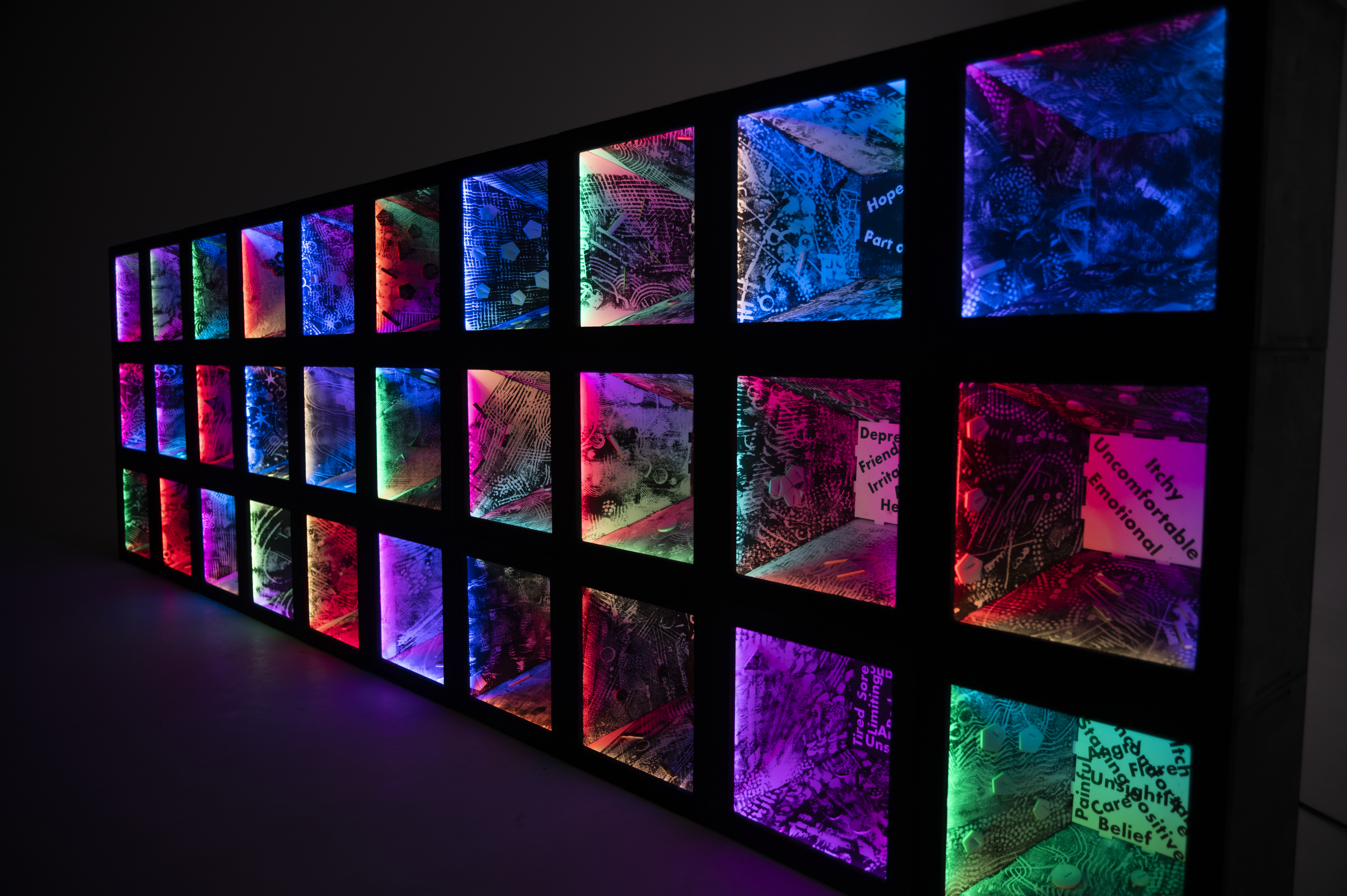 Sculpture created by Julia Vogl and Peter Hudson, in collaboration with participants of the 'Colouring Adult Eczema' project. 30 illuminated boxes, lit in different colours and marked with various patterns are stacked on each other to form a wall.