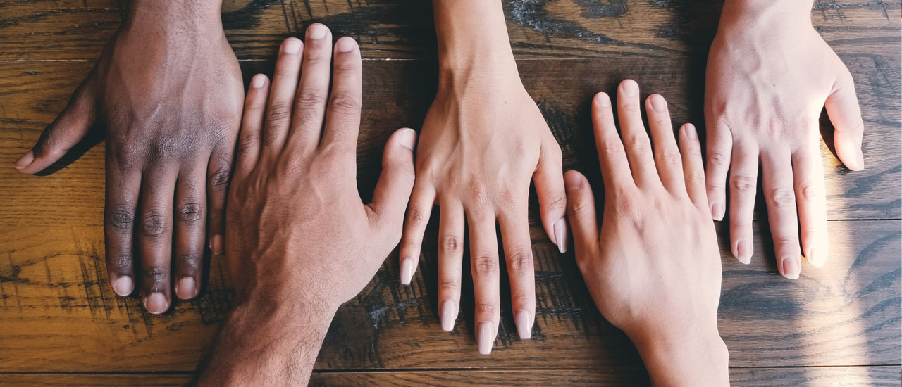 Hands of five people with different ethnicities facing down on a table. Credit: Clay Banks via Unsplash