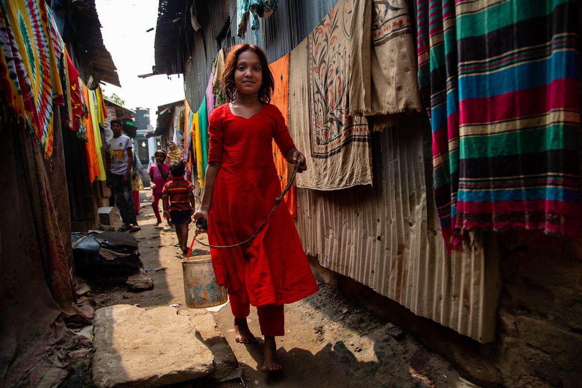 A young girl carries a bucket of water drawn from a well in a slum