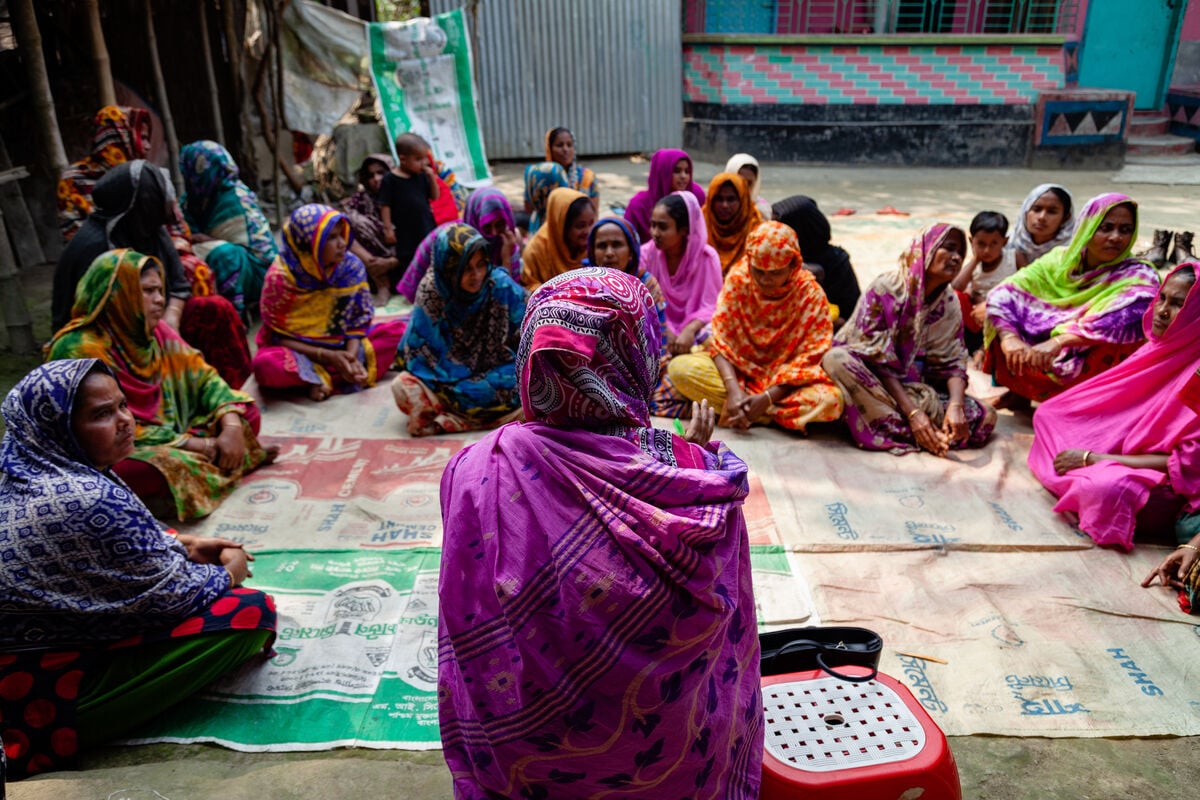 A group of women sit on the mats on the ground together during a meeting discussing health impacts of a Polio vaccination