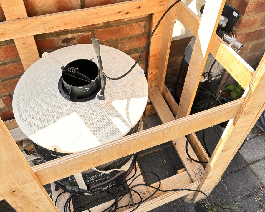 Image of a cylindrical object set within a wooden frame on the ground to trap mosquitos