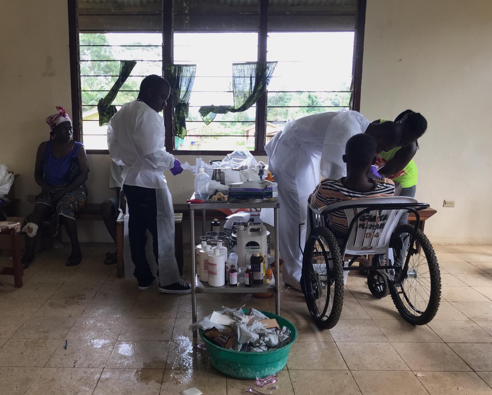 Nurses clean the wounds of a man affected by Buruli ulcer who recently arrived from the community after receiving traditional medicine with no improvement. A family member helps to keep the patient still while nurses remove mud and leaves to clean the ulcers.