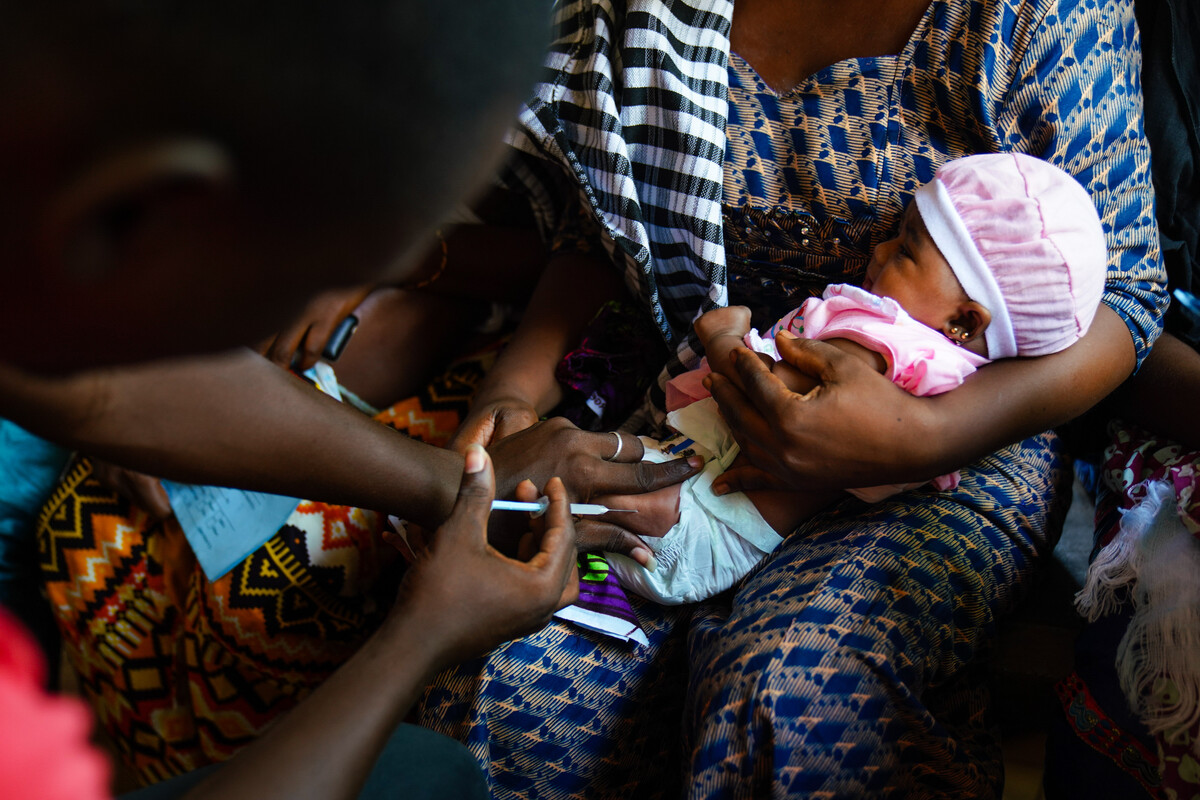 image of a baby being held by its mother, while someone prepares a vaccine