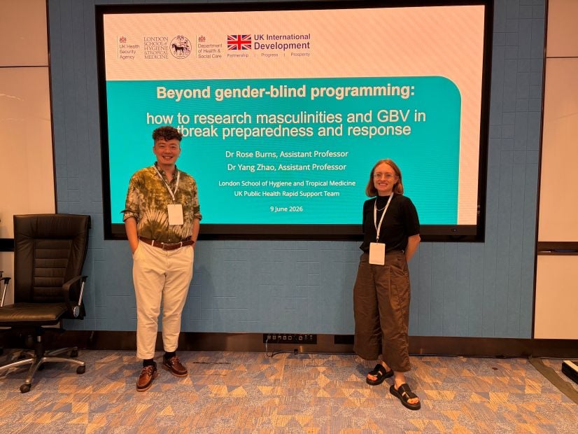 Two people smiling standing in front of digital screen showing presentation. 