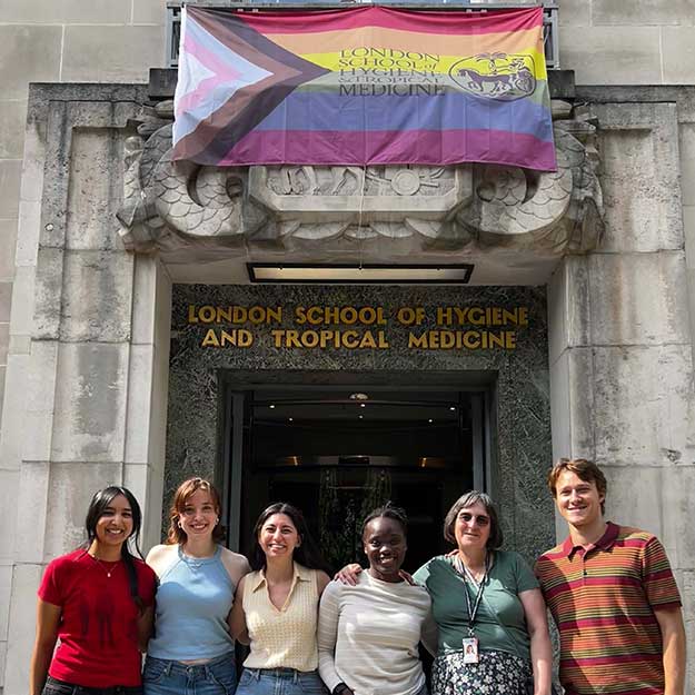 Alejandra (centre) wearing a yellow top and jeans stands outside the LSHTM entrance with five classmates.