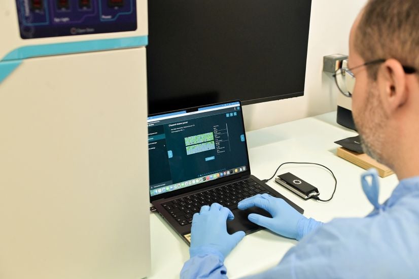 Person in lab working on computer with gloves on.