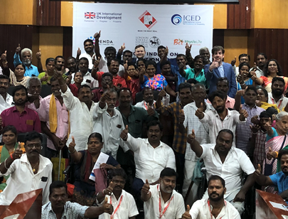 Attendees from the in-person dissemination event for the De-Worm study in India pose for a photo in front of the conference banner. Most people have their arms raised showing the 'thumbs up' sign.
