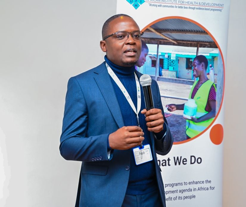 Kenyan advocate standing next to a banner talking into a microphone at UK-PHRST Kenya Disability Study workshop