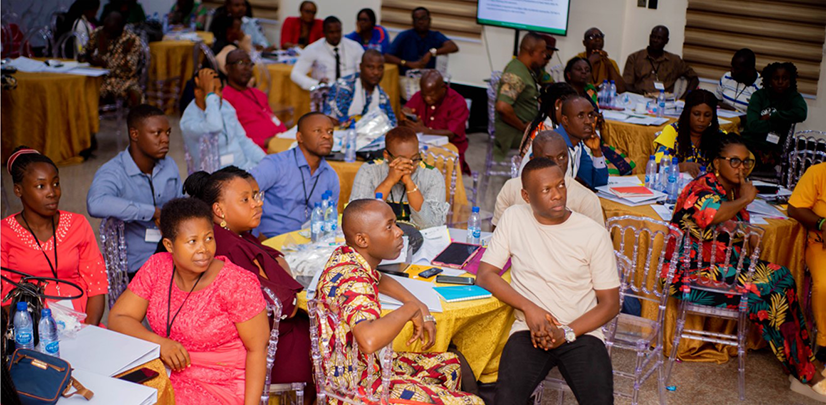 Workshop attendees sitting around tables watching presentation, dressed in colourful clothes