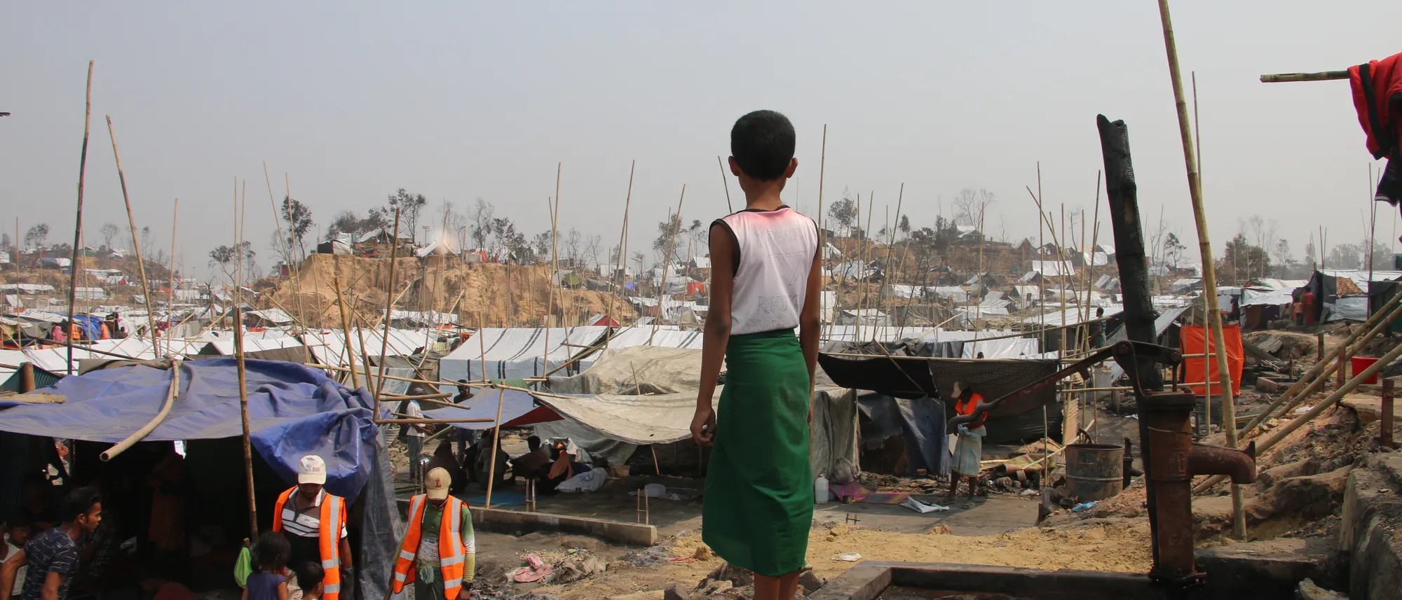 Boy looks over a refugee camp of makeshift coverings held up by sticks. Image credit: Ummay Habiba/Save the Children