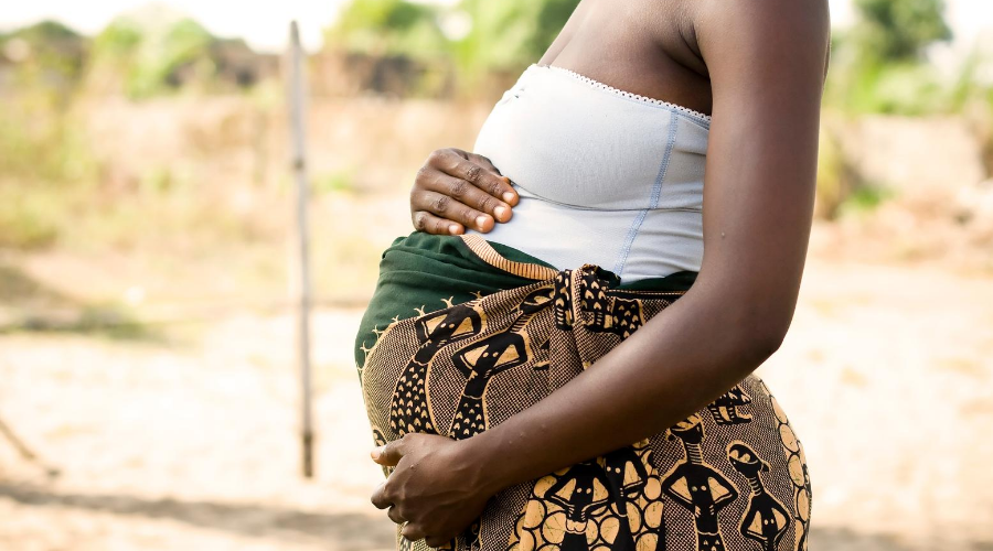 Side view of pregnant woman in Africa wearing white top and patterned skirt, cradling her bump
