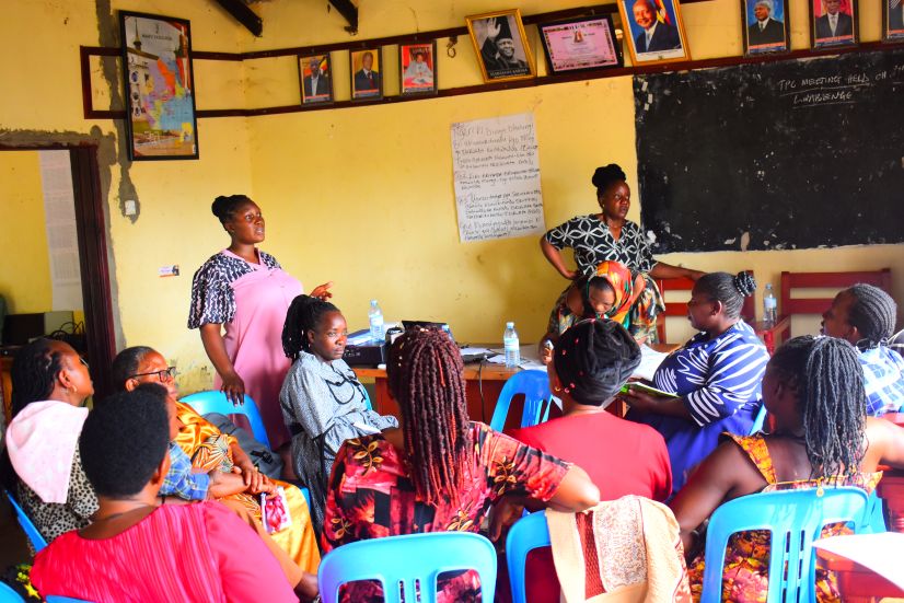 Women delivering training in Uganda, standing in front of a classroom with seated audience listening