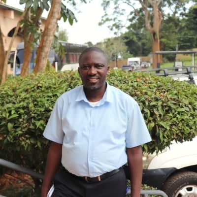 Robert is wearing a light blue shirt and standing on the stairs outside. Some buildings and parked cars are visible behind him.