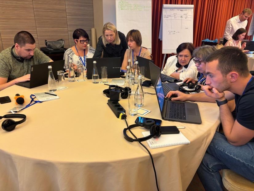 Workshop attendees sitting around tables and working at laptops.
