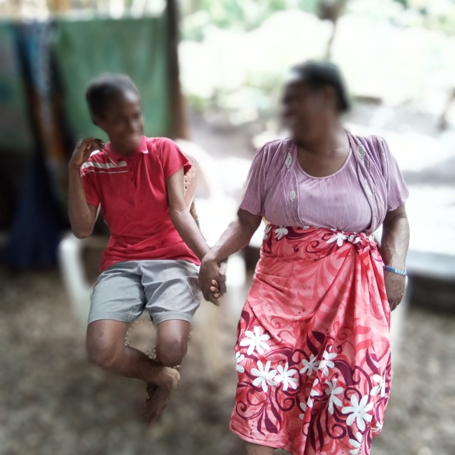 A woman and a girl sitting on chairs beside each other and holding hands. Their faces have been blurred out for privacy.