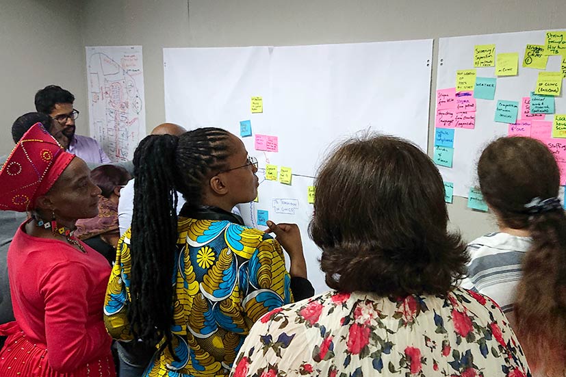 people standing looking at paper on wall, adding notes to make a theoretical model