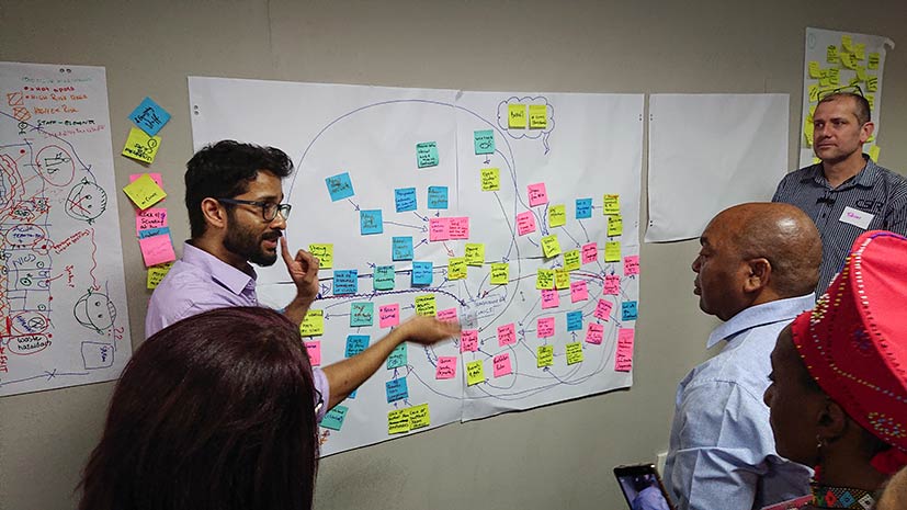 man standing in front of chartboard paper explaining model and post-it notes to people
