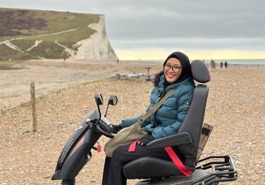 Luthfi is at the Seven Sisters cliffs wearing a puffer jacket and sitting on a mobility scooter.