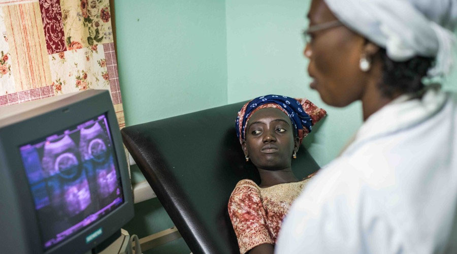 Woman laying down on hospital bed whilst female nurse looks at scan image on screen, MRC The Gambia