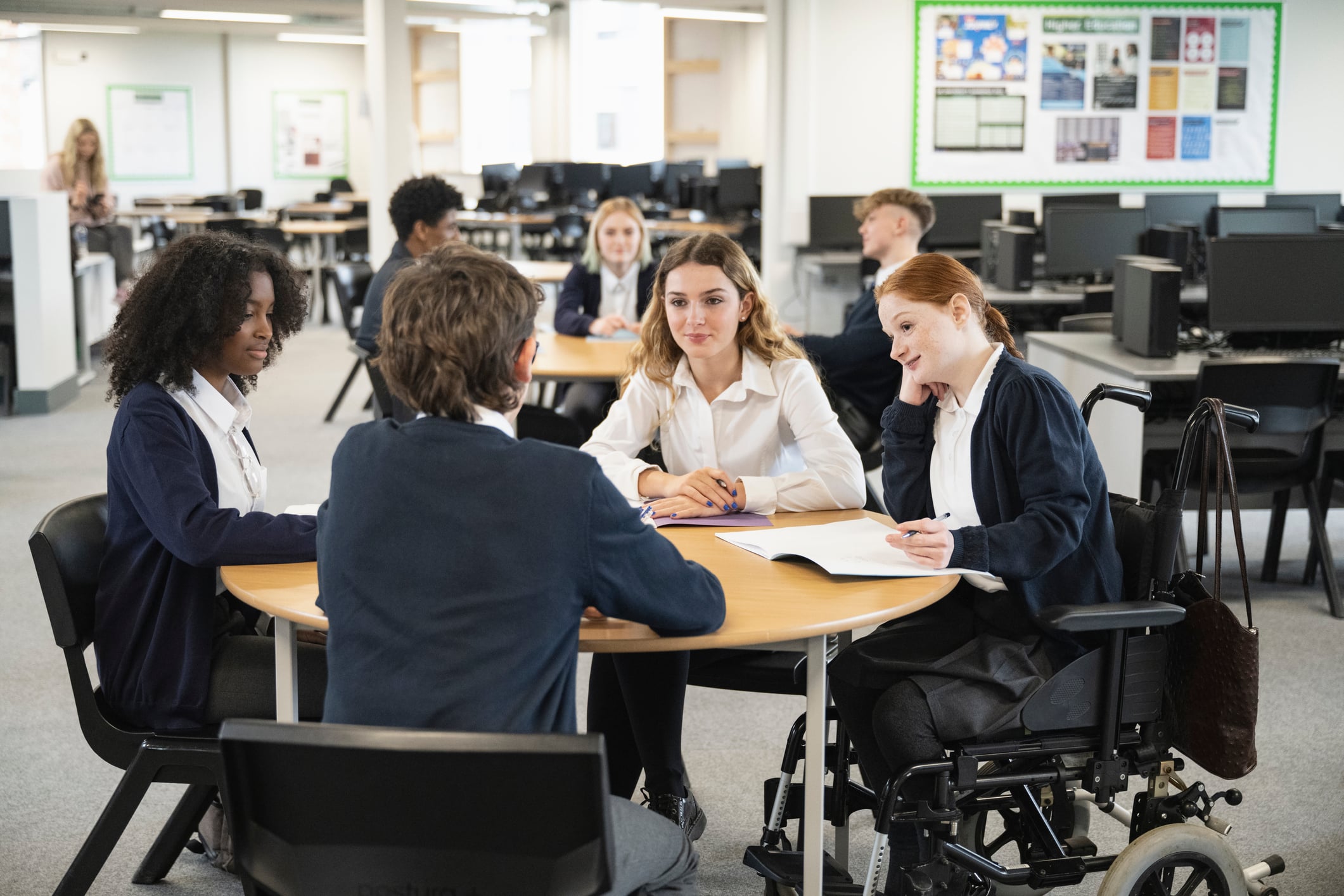 A group of young people sit around a table at school discussing work.