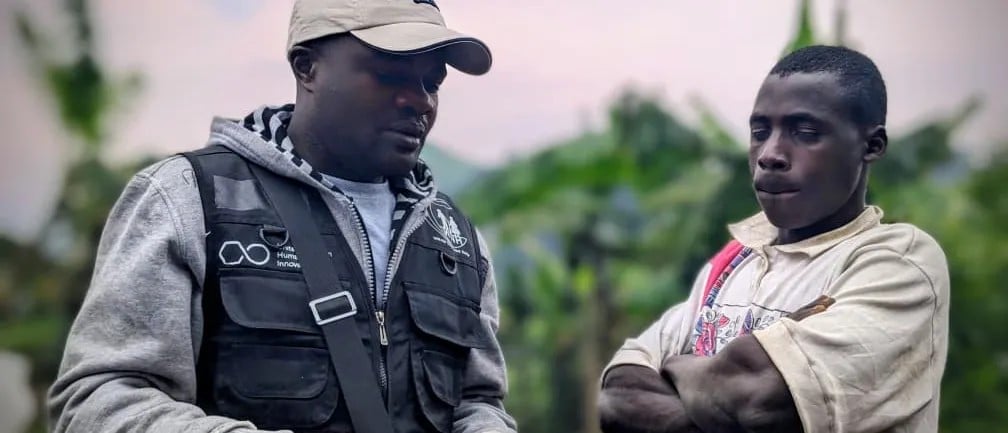 Two African men are having a conversation. Their eyes are downcast. One of them is wearing a vest that says the Humanitarian Systems Innovation Hub. Image credit: Saeed Rahman