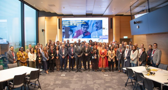 About twenty men and women pose in front of screen in large conference room