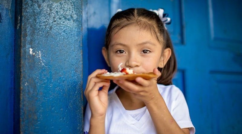 A girl eats toast in front of a blue door