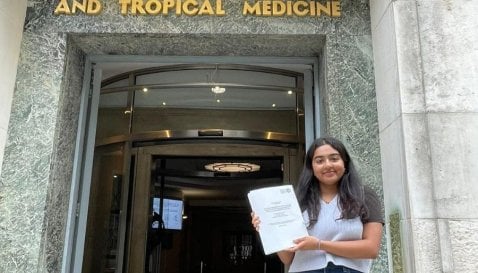 Student, Adhishree, stood outside the LSHTM building holding their dissertation.