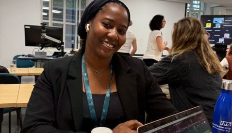 Student, Hassana, in a classroom smiling to camera with other students studying behind her.
