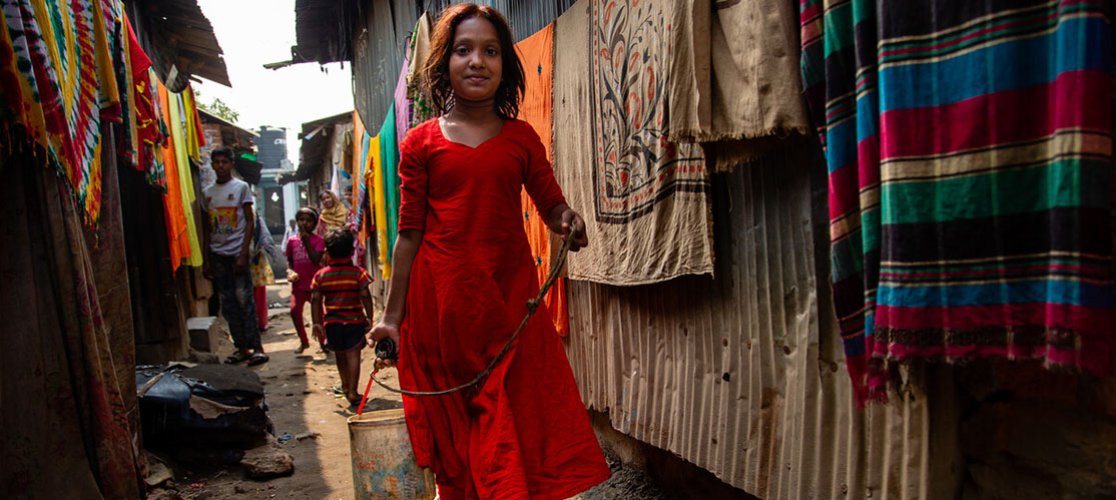 A young girl carries a bucket of water drawn from a well in a slum