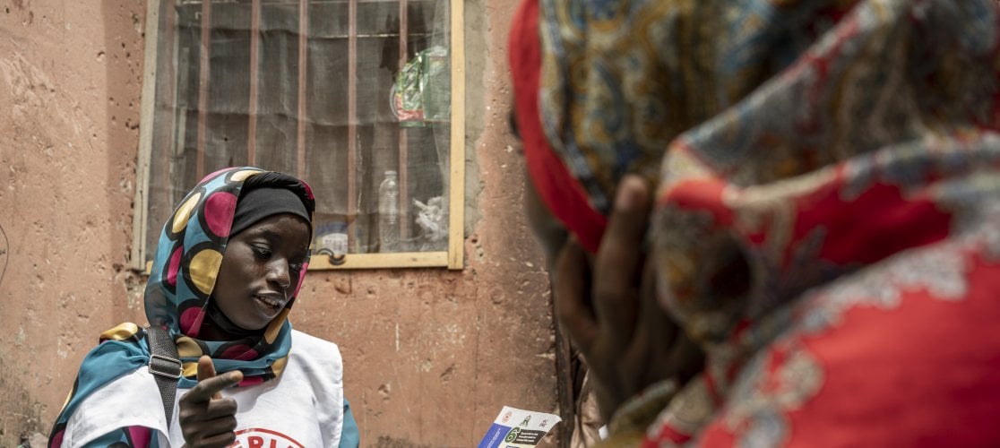 Salma, a community volunteer with the Nigerian Red Cross speaks to a mother during a community engagement for diptheria in Kano