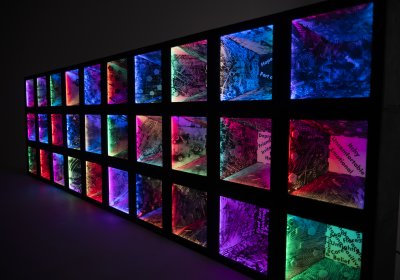 Sculpture created by Peter Hudson and Julia Vogl in collaboration with participants of the 'Colouring Adult Eczema' project. 30 illuminated boxes, lit in different colours and marked with various patterns are stacked on each other to form a wall.​ 