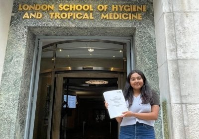 Student, Adhishree, stood outside the LSHTM building holding their dissertation.