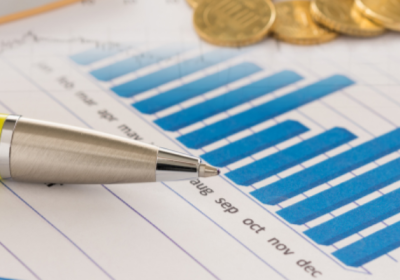 Picture of a pen and pile of coins on top a notebook with a graph