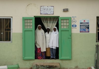 Three healthcare professionals at entrance to maternity ward, Gombe State Nigeria. Credit: IDEAS