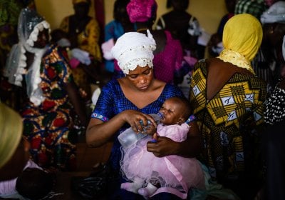 Woman holding a child, sitting down in a crowded area.