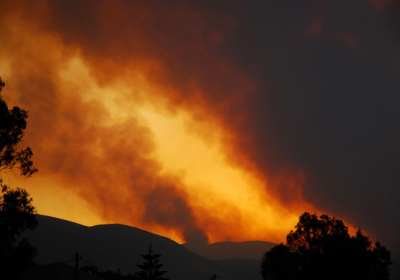 Image of an mountain side in dark silhouette with orange sky and large plumes of thick grey smoke rising into the air