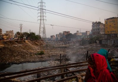 	A woman crosses a bridge spanning a dry riverbed and covers her face from the fumes of burning rubbish, Dhaka