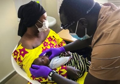 n infant, carried by his mother, being examined by a male nurse.