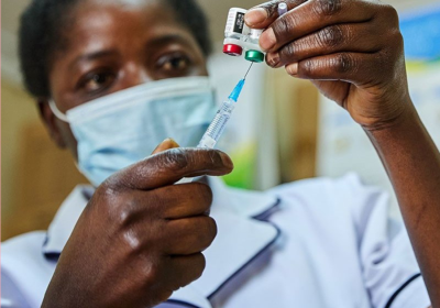 Health worker in mask draws a dose of RTS,S malaria vaccine from a vial into a syringe. 