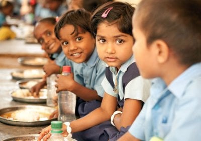 School children in India sit at a bench to eat their midday meal