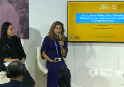 Two women sit on chairs in front of a screen with a presentation title