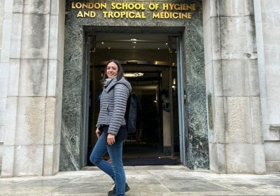 Person stood outside on the steps outside LSHTM entrance wearing a grey coat.