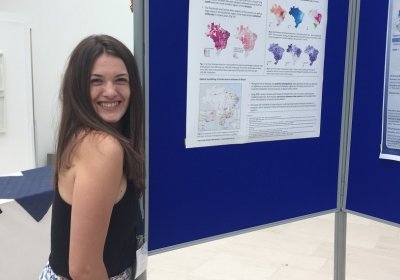 Sophie in front of a poster of her research which focuses on dengue in Brazil