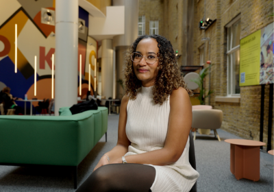 Alumna, Megan, sits in social space within LSHTM wearing a cream dress.