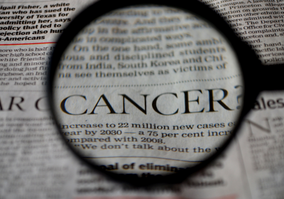 A magnifying glass hovering over a newspaper and the word CANCER is magnified